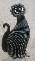 Full front and side view of the black and white striped Murano glass cat figurine on a textured beige background.
