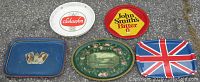 All five vintage tin beer trays arranged on the floor showing various colors and designs including logos and flags.