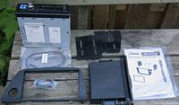 Photo showing Alpine car radio model CDE-100 with mounting parts and instruction manual laid out on wooden surface outdoors.