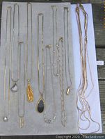 10 gold-tone chains arranged on a light gray surface showing varying pendant styles and chain designs.