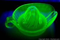 Juicer reamer glowing bright fluorescent green under UV light to verify Vaseline glass authenticity.