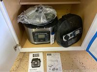 Pressure cooker stored inside a cupboard, includes control panel and owner's manual placed below the unit.