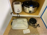 Photo showing all four items together: Pampered Chef tray, Hamilton Beach slow cooker, Perfect Cooker rice cooker, Crock Pot Little Dipper slow cooker.