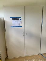 Full view of closed white Closetmaid wardrobe cabinet with two doors and silver handles.