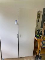 Closed white wardrobe and storage cabinet with two doors and simple handles.