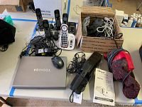 Photo showing Toshiba laptop, multiple Panasonic cordless phone handsets, cords, Royal Hand Vac, and manual on table.