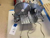 Full view of electric meat slicer showing circular blade, metal carriage for meat, and power cord.