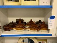 Shelf display of nine soup crocks, eight with lids, one without lid visible from the front.
