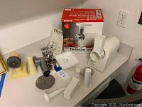 Full view of all components including main unit, feeding tray, multiple metal grinder plates, plastic stomper, instruction manual and original box shown on top of a surface.