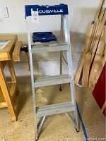 Front view of Louisville 4 ft aluminum step ladder, showing three wide steps and blue tool tray at top.