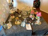 Photo showing various glass and ceramic tabletop decorative pieces on a grey cloth, including animals and flowers.