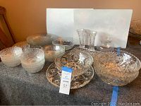 Set of multiple glass bowls, a matching glass platter, and two Lenox crystal bud vases displayed on a grey cloth.