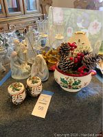 Photo showing white ceramic nativity music box, praying Mary figure, holly salt and pepper shakers, floral ceramic candle holder with pine cones and berries