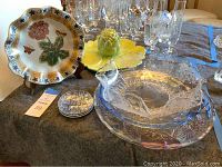Photo of various glass platters, decorative plates, and a fluted glass bowl on a table.