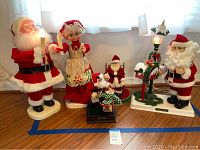 Full group photo of six holiday-themed animated and decorative figures placed against wall with kitchen window in background.