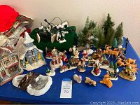 Photo showing assorted Christmas villagers, animals, houses, and trees arranged on blue surface.