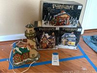 Set of four Victorian Village Collectibles Christmas village buildings shown together including one unboxed lighthouse house with attached green roofed house and three boxed buildings.