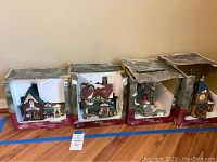 Four boxed Holiday Time Village Collectible buildings including florist, grocery, grist mill, and church, each about 8 to 10 inches tall, displayed on wooden floor