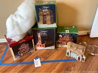 Porcelain village houses in original boxes along with one loose porcelain lighted house with a thatched roof, wired for power.