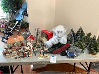 Wide shot showing an assortment of Christmas village figurines, light posts, snow decorations, trees, and houses arranged on a table.