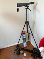 Bushnell Elite 70 monocular mounted on adjustable tripod with lens cover, standing on floor.