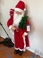 Front view of large Santa figurine dressed in red holding Christmas tree and candy cane