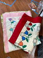 Pair of folded vintage quilts showing applique tulip designs and pink gingham pattern with floral backing.