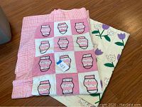 Two vintage quilts folded, showing pink mittens on checked background and tulip flowers on cream background.