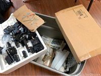 Box with multiple quartz clock movements and assorted clock hands on cardboard in packaging