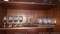 Shelf holding the full set of clear etched glassware including stemmed wine glasses, tall bud vases, short parfait glasses, and a serving piece.