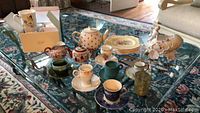 Wide photo showing various ceramic items on table including cups, plates, teapot, figurines