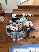 Overview of assorted coffee mugs, pitchers, Mickey Mouse cake mold, several baking pans, and ornate metal candelabra placed on floor.