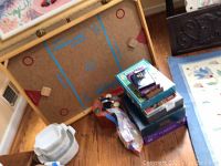 The tabletop Nok Hockey board with two wooden puck stops and multiple stacked board game boxes beside it.