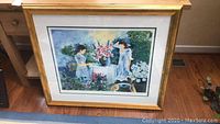 Framed wall art featuring two girls in a garden with a floral centerpiece, gold frame.