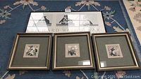 Four pieces of framed wall art lying on a blue rug, including three floral paintings with decorative frames and one rectangular framed print behind them.