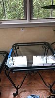 Front view of the glass top side table showing clear glass surface and black metal frame with scrollwork.