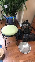 Full view of the antique chair with black metal frame and light green upholstery, along with black metal candle holders and a metal tray placed on wooden floor.