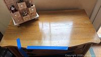 Top surface of wood cabinet showing scalloped edge and light surface wear with blue tape marking.