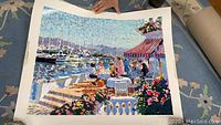Large colorful print of a waterfront scene with people dining near boats
