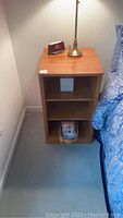 Night stand shown next to a bed with a lamp and clock on top, detailing size and condition of surface.