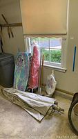 Photo showing boogie boards leaning against wall with umbrellas and poles beside them, including folded canopy fabric and umbrella stand base.