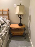 Full view of side table with picnic basket underneath and table lamp on top, placed next to bed.