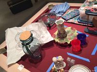 Overview of all items including glass bowl, vases, glasses, jars, and plates arranged on a table with some wrapped in packing materials.