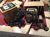 Panasonic Newvicon OmniPro video camera PK957 with original box and instruction manual, Bell and Howell 253A projector with reels and cords, and Polaroid SX-70 Land Camera on tabletop.