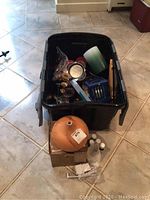 Plastic bin filled with various items including brass candlestick holders, candles, blue candle holder, small photo stand, and diffuser.