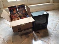 Symphonic black combo TV and VCR unit beside box of Disney VHS tapes on tiled floor.