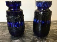 Front view of two matching black and blue lava-glaze vases side by side