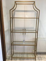 Full front view of gold metal and glass etagere with plastic water bottle on third shelf for scale