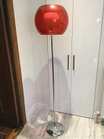 Full-height view of lamp against wall showing red globe shade, chrome pole and base