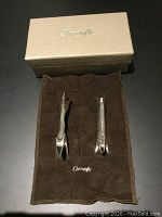 Two silver-plated utensil rests shaped like a fox and a rabbit laid on brown Christofle pouch alongside beige box with Christofle logo.